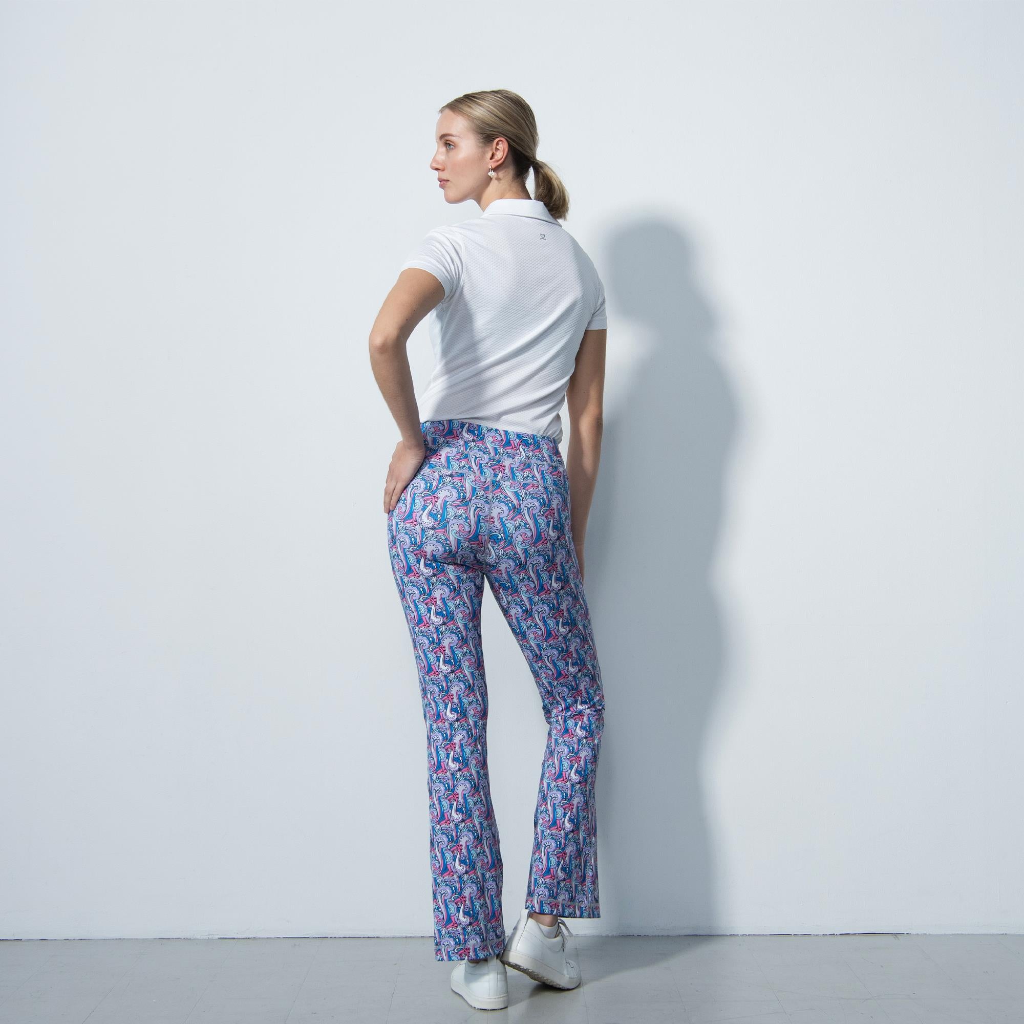 Back shot of blonde model in a white polo shirt and flared patterned trousers taken in a photography studio 